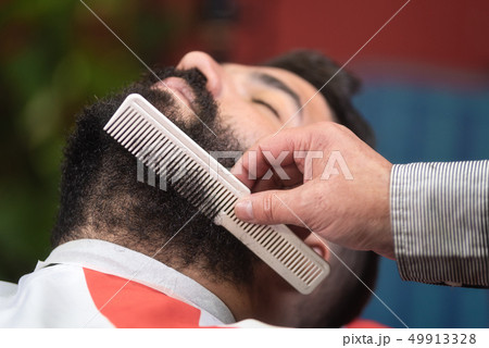 Barber making beard haitstyle using comb at barber shop. 49913328