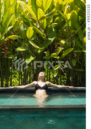 Sensual young woman relaxing in outdoor spa infinity swimming pool surrounded with lush tropical 49920330