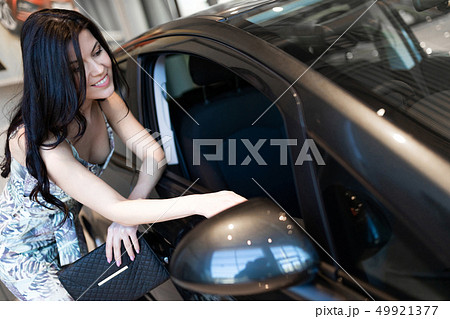 Beautiful fashionable brunet possing near her new car in dealership showroom 49921377