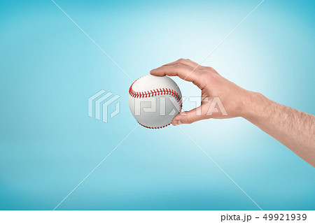 Side view of man's hand holding white baseball on light-blue background with some copy space. Side view of man's hand holding white baseball on light-blue background with some copy space. 49921939