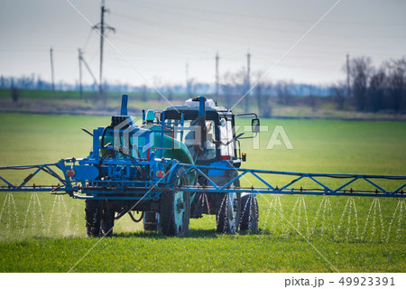 Blue tractor with spraying device in green field Blue tractor with spraying device in green field 49923391