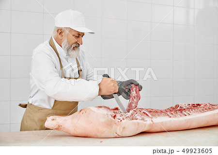 Elderly butcher slicing fresh meat on table of butchery. Elderly butcher slicing fresh meat on table of butchery. 49923605