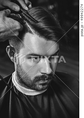 Young handsome barber making haircut for attractive man in barbershop 49942274