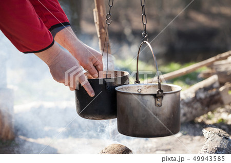 Man cooking in sooty old pots on bonfire Man cooking in sooty old pots on bonfire 49943585
