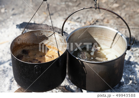 Cooking in two sooty old cauldrons on campfire 49943588