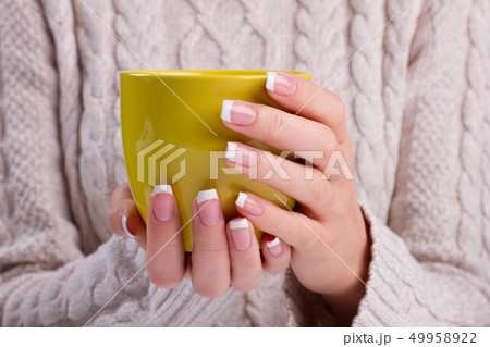 Hands with french manicure holding a yellow mug. 49958922