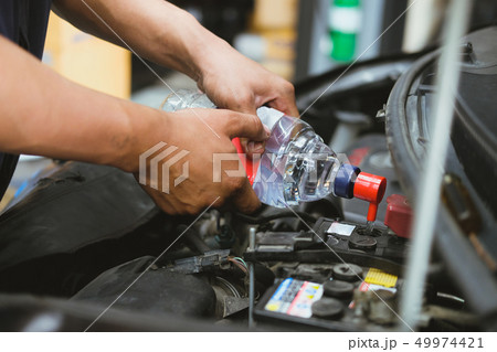 mechanic pouring distilled water to fill car battery in automobile repair service 49974421