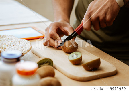 Close up of dark-skinned man cutting kiwi for fruit salad Close up of dark-skinned man cutting kiwi for fruit salad 49975979