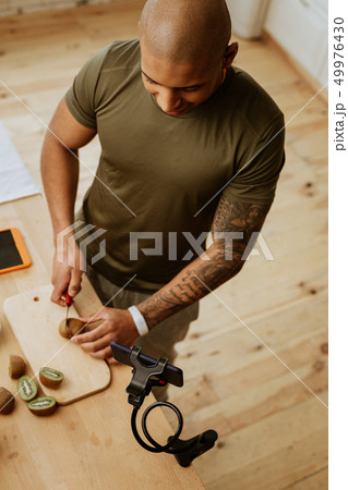 Sportsman with tattoo cutting kiwi while filming video about food 49976430