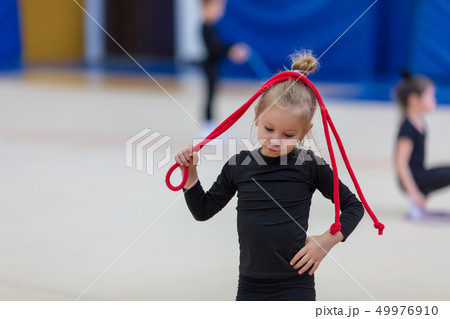 little gymnast is holding the rope over her head while exercising 49976910