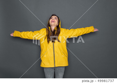 Cropped photo of happy Caucasian girl wearing yellow raincoat against gray background Cropped photo of happy Caucasian girl wearing yellow raincoat against gray background 49981737