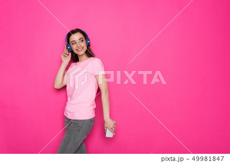 Cropped photo of cheerful brunette Caucasian girl wearing headphones against pink background Cropped photo of cheerful brunette Caucasian girl wearing headphones against pink background 49981847