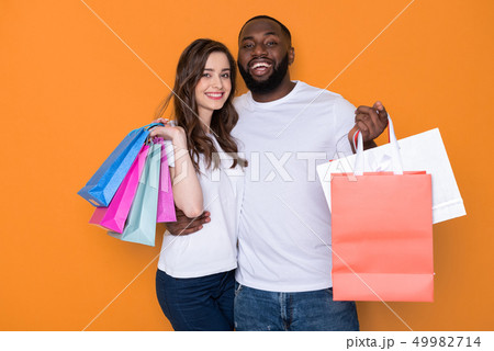 Happy interracial couple in white T-shirts posing for camera in studio Happy interracial couple in white T-shirts posing for camera in studio 49982714