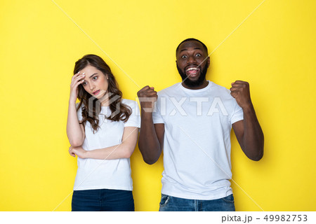 Young interracial couple in white T-shirts posing for camera in studio Young interracial couple in white T-shirts posing for camera in studio 49982753