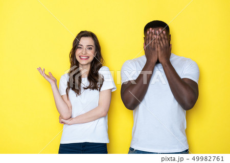 Young interracial couple in white T-shirts posing for camera in studio Young interracial couple in white T-shirts posing for camera in studio 49982761