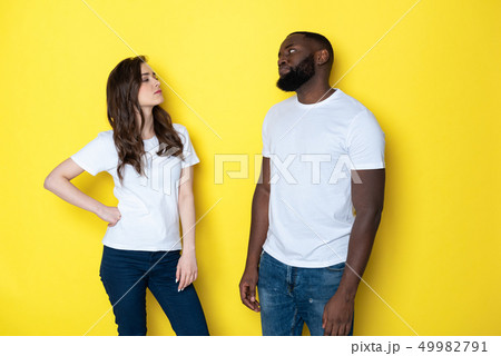 Unhappy interracial couple in white T-shirts posing for camera in studio Unhappy interracial couple in white T-shirts posing for camera in studio 49982791