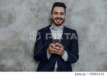 Happy elegant man with smartphone against grey wall 49984143
