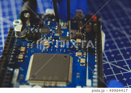 Microcircuit with tweezers on the background of electronic components Microcircuit with tweezers on the background of electronic components 49984417