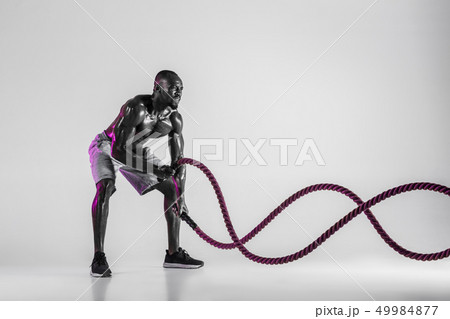 Young african-american bodybuilder training over grey background 49984877