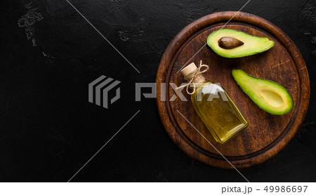 Two avocado halves and bottle of oil on board 49986697
