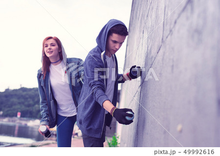 Inspired dark-haired guy being graffiti artist and painting concrete surface 49992616