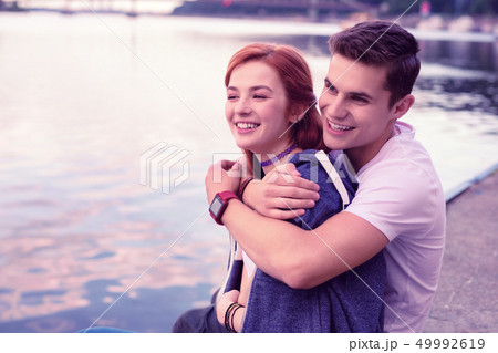 Strong smiling guy tightly hugging his pretty ginger girlfriend 49992619