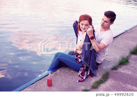 Short-haired young man in white t-shirt sharing his warm hoodie with cold girlfriend 49992620