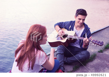 Inspired good-looking guy sitting on the ground with acoustic guitar 49992621