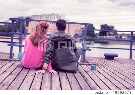 Smiling ginger girl in pink hoodie sitting close to her short-haired boyfriend 49992673