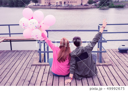 Long-haired ginger girl carrying bunch of balloons while resting on the wooden surface 49992675