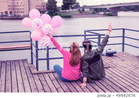 Excited young pretty couple sitting together on the river coast 49992676