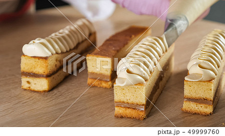 Pastry chef decorates biscuit with cream from pastry bag. Pastry chef decorates biscuit with cream from pastry bag. 49999760