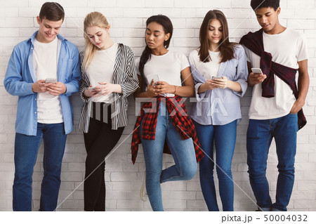 Students texting on their smartphones, leaning on wall 50004032