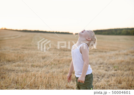 Happy blond boy stands with his head up on a mown Happy blond boy stands with his head up on a mown 50004601