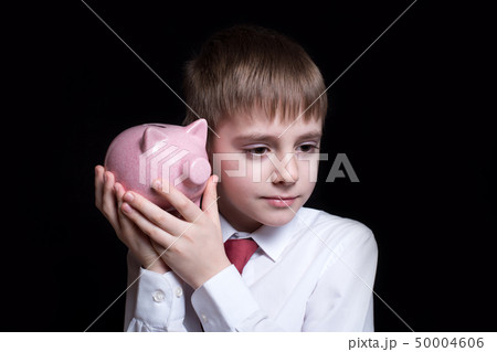 Boy listens attentively to the pink piggy bank. 50004606