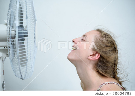 Young woman sitting under a fan with closed eyes 50004792