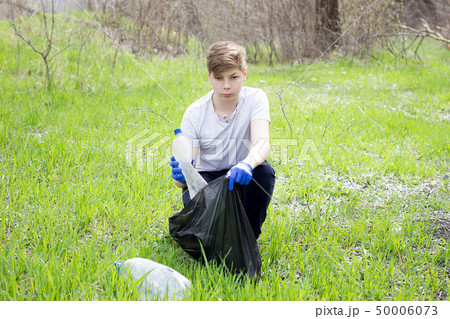 guy volunteer picks up trash on green grass.  50006073