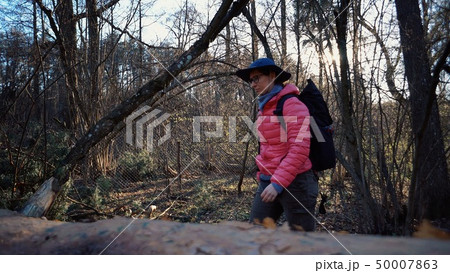 Young woman tourist with a backpack steps over a fallen tree in the forest with a backpack. Theme 50007863