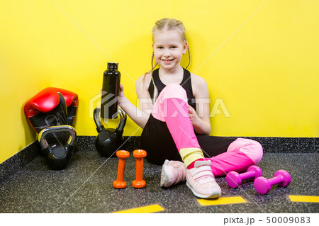 Theme sports and health children. Little Caucasian girl sits resting break floor gym holds hand Theme sports and health children. Little Caucasian girl sits resting break floor gym holds hand 50009083