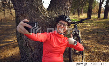 Young caucasian woman athlete tourist cyclist uses hand smart phone photo of herself selfie sitting 50009132