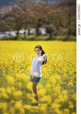 奈良県橿原市の藤原宮跡の菜の花畑を背景にしているショートパンツ姿の笑顔の若い女性 50020687