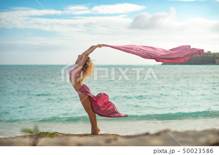 Fit and sporty young girl posing on a beach with pink flying silk 50023586