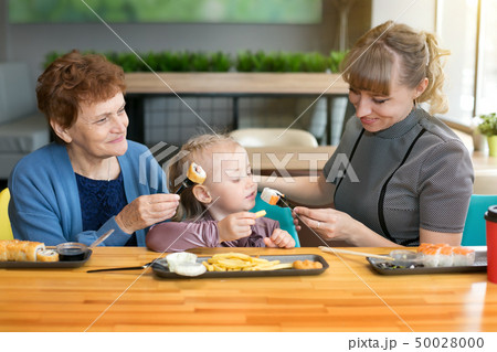 Grandmother and mother feed the little girl in Grandmother and mother feed the little girl in 50028000