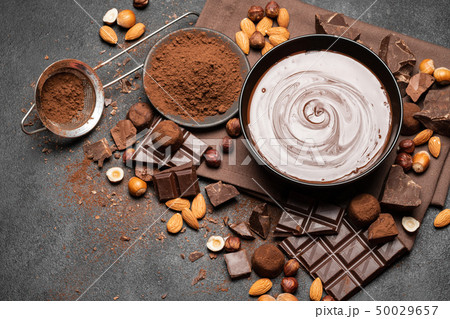 ceramic bowl of chocolate cream or melted chocolate, nuts and pieces of chocolate on dark concrete 50029657