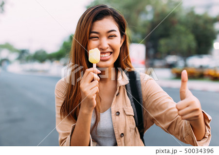 Young woman showing thumbs up with popsicle ice cream in outdoor scene 50034396