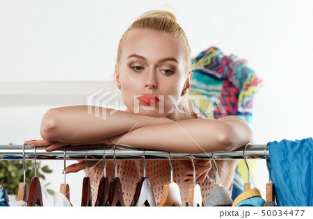 Beautiful blonde woman standing near wardrobe rack 50034477