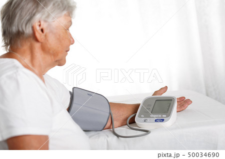 Elder woman measuring blood pressure with automatic manometer at home 50034690