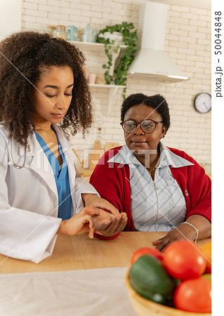 Caregiver wearing white jacket measuring pulse for woman 50044848