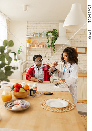 Nurse in white jacket coming to kitchen and measuring blood pressure Nurse in white jacket coming to kitchen and measuring blood pressure 50044933