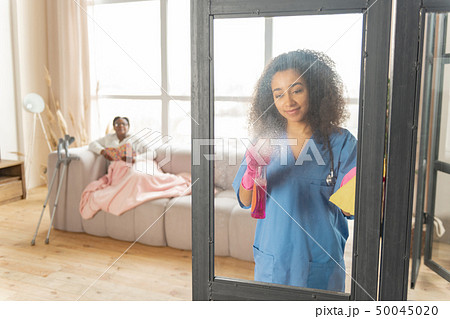 Nurse cleaning the glass door in the living room of patient Nurse cleaning the glass door in the living room of patient 50045020
